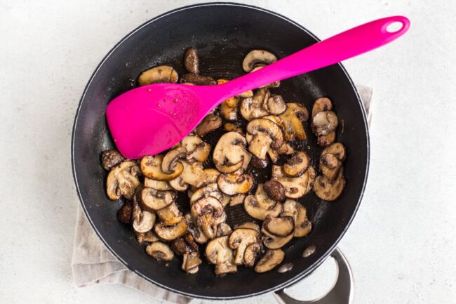 Garlic mushrooms cooking in a frying pan.