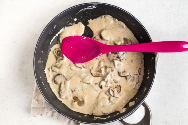 Creamy garlic mushroom sauce cooking in a frying pan.