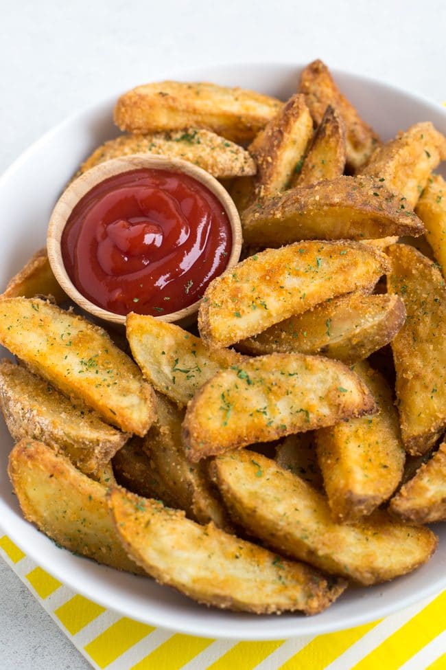 Crispy potato wedges in a bowl with a pot of ketchup
