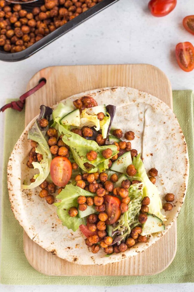 A flour wrap on a wooden chopping board, topped with salad and spicy roasted chickpeas.