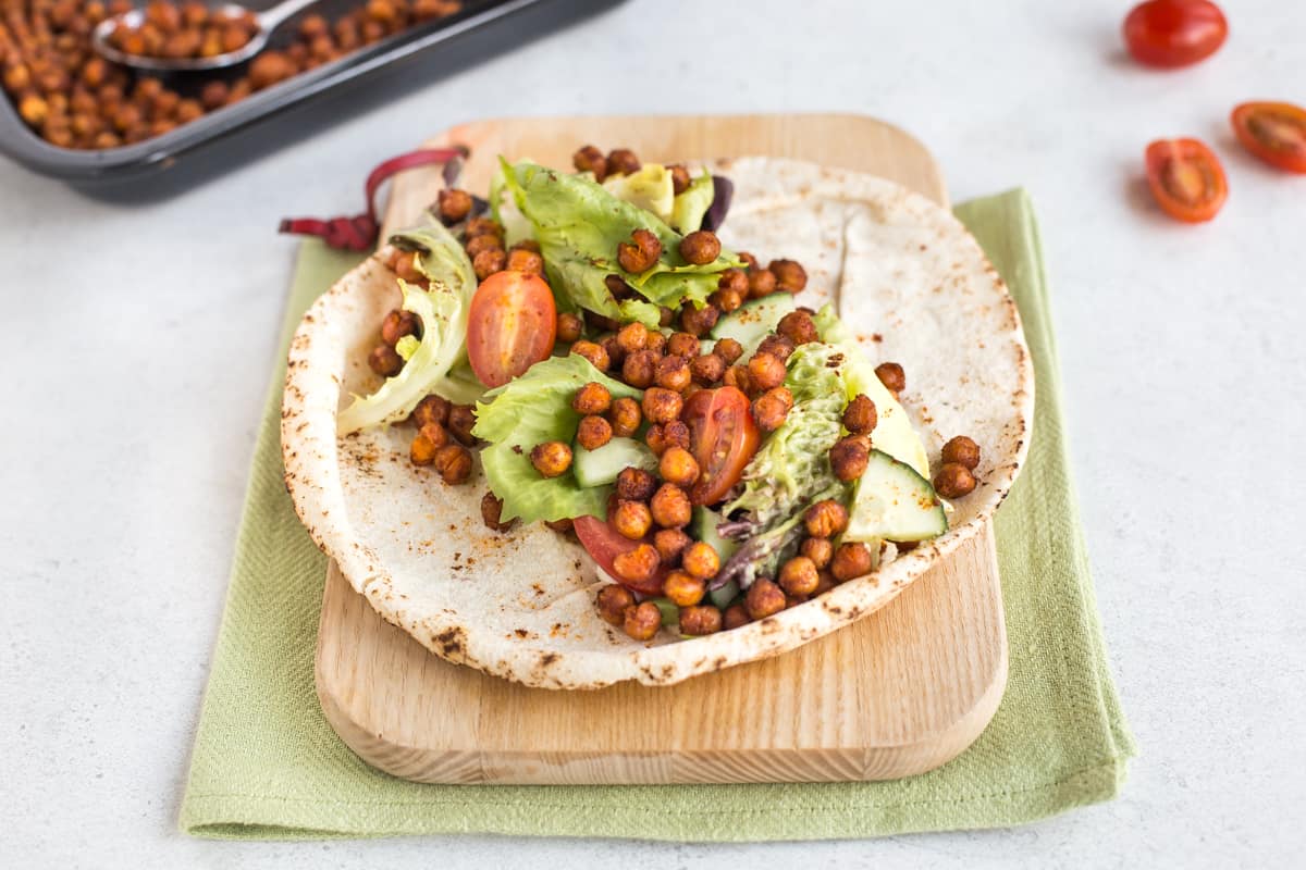 A wrap on a wooden chopping board, topped with salad and spicy roasted chickpeas.