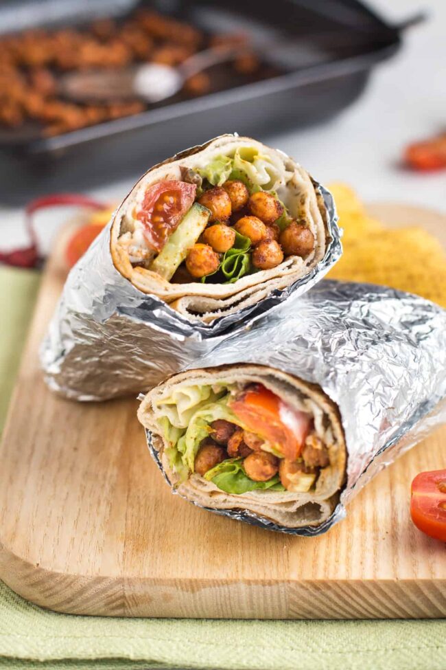 A spicy roasted chickpea salad wrap on a board, wrapped in foil.