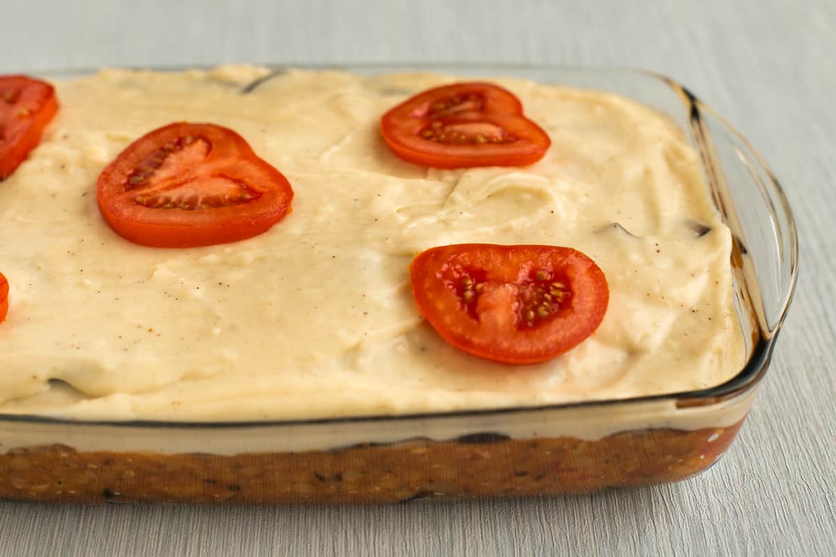 An uncooked vegetarian moussaka in a baking dish topped with sliced tomatoes.