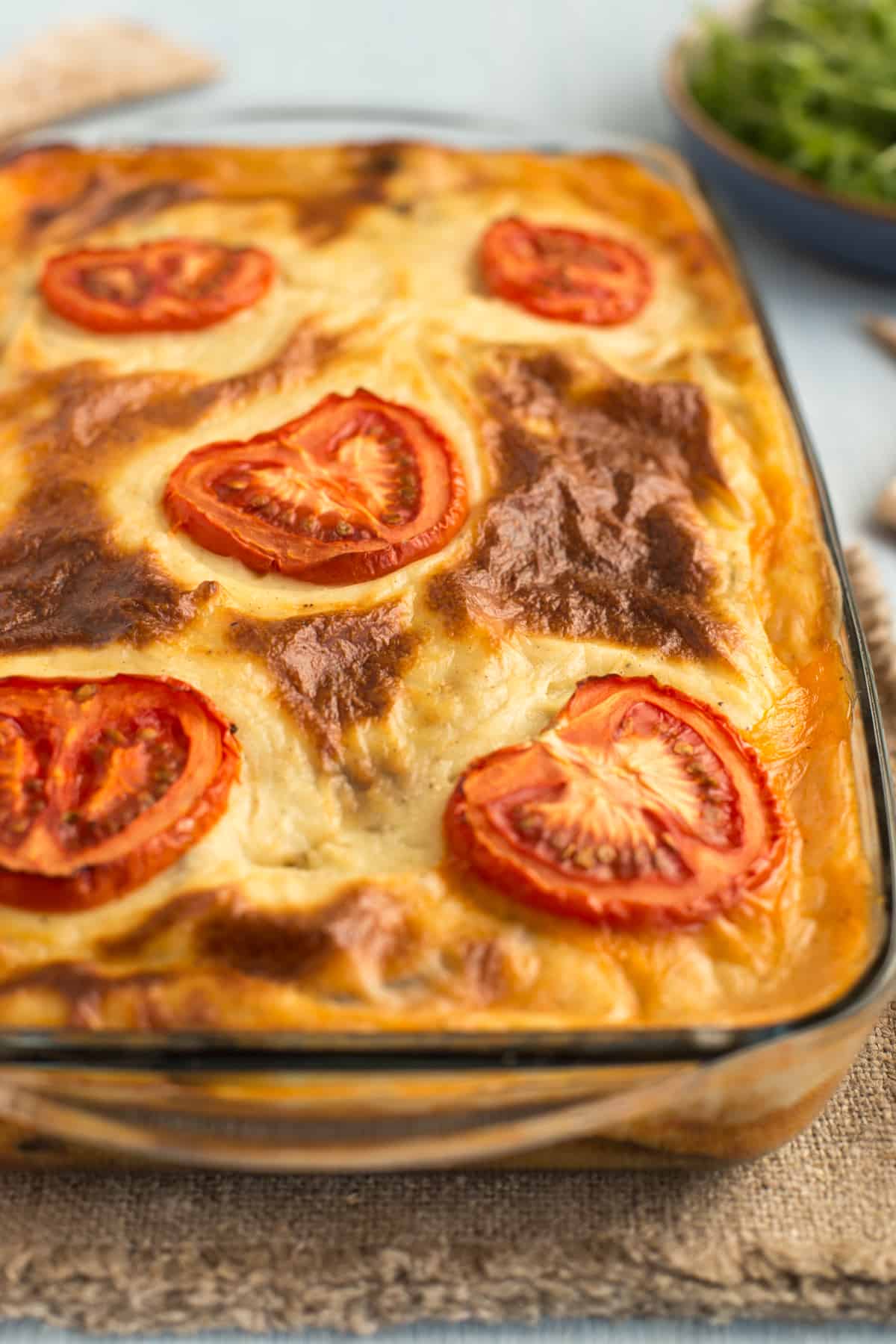 A baked vegetarian moussaka in a baking dish, topped with sliced tomatoes.