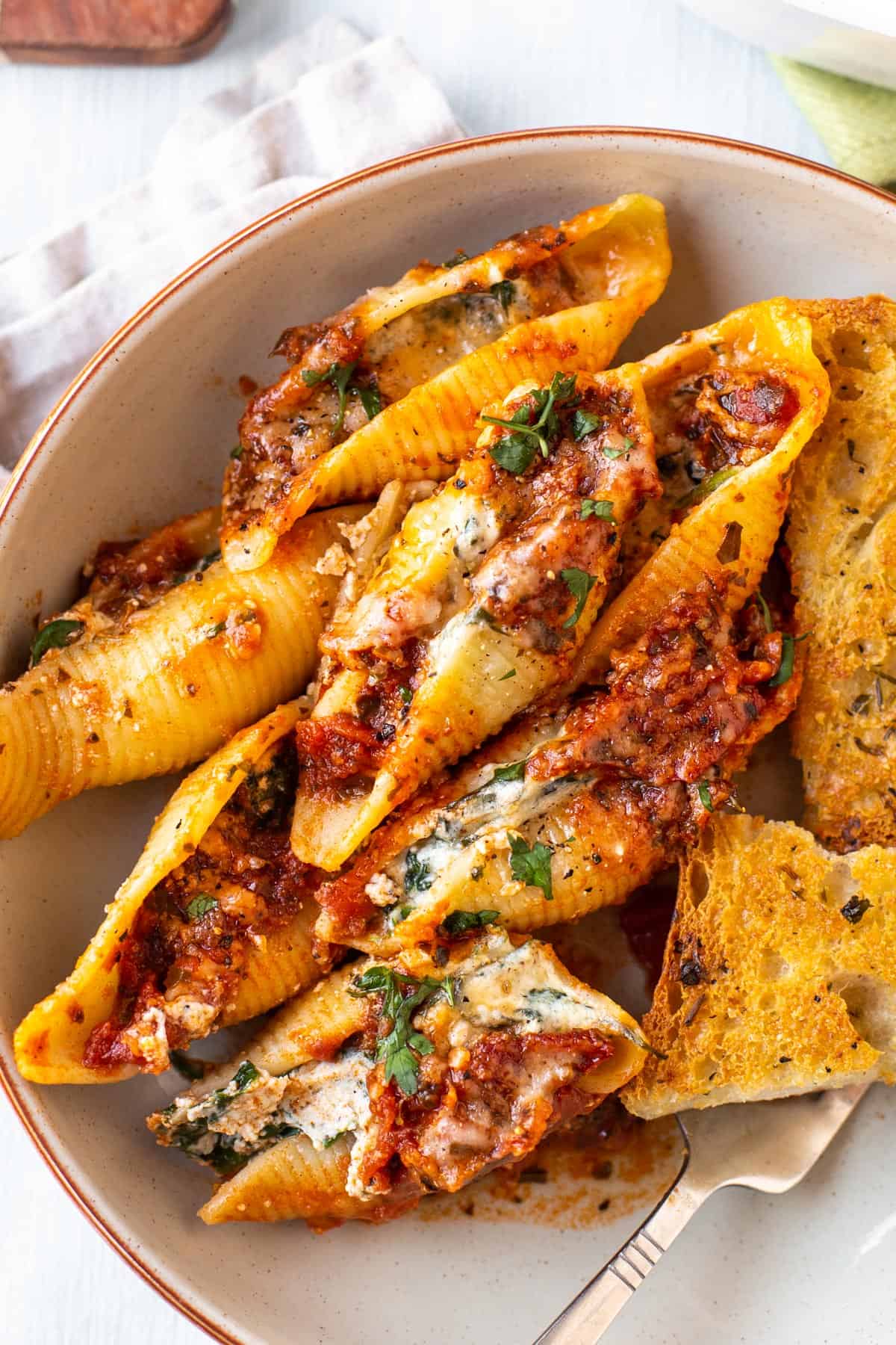 A portion of cheesy spinach stuffed shells in a bowl with garlic bread.