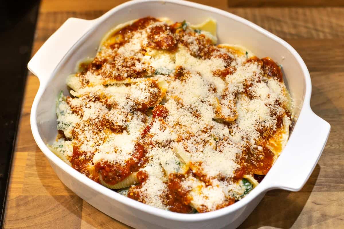 Stuffed pasta shells in a baking dish topped with grated parmesan cheese, ready for baking.