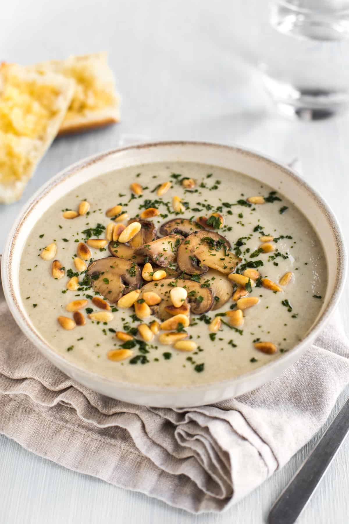 Bowl of creamy vegan mushroom soup topped with garlic sautéed mushrooms and toasted pine nuts.