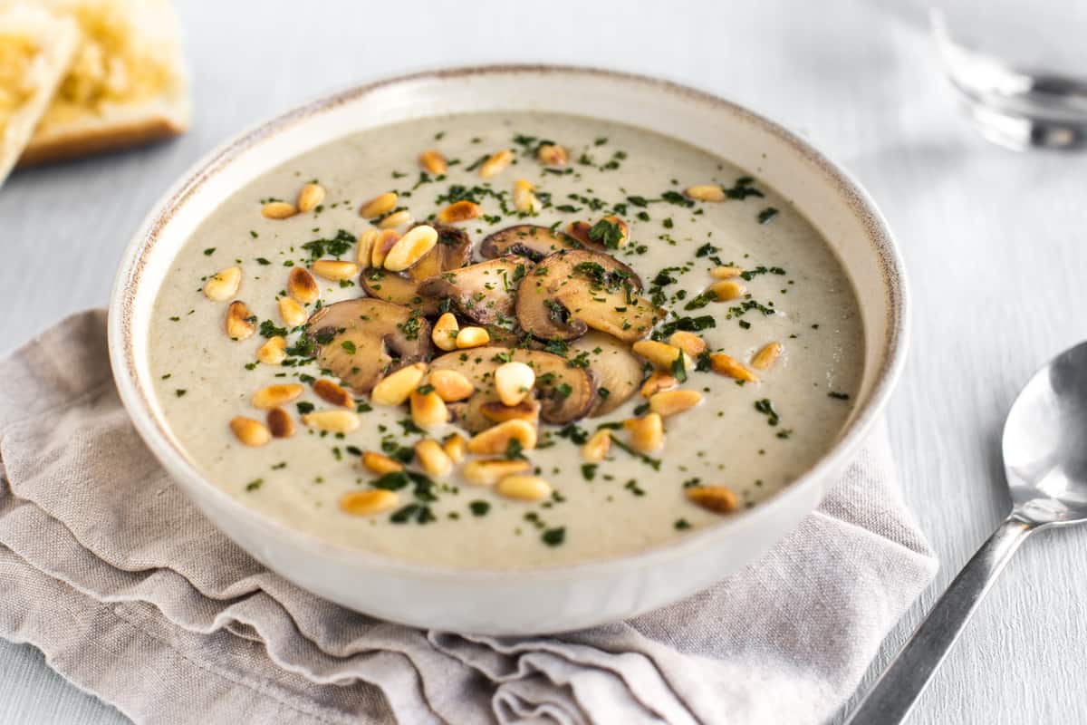 Bowlful of creamy mushroom soup topped with mushrooms and toasted pine nuts.