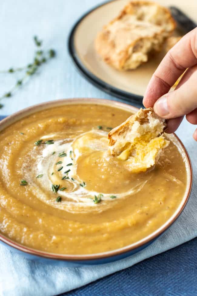 A hand dipping some crusty bread into a bowl of creamy parsnip soup.