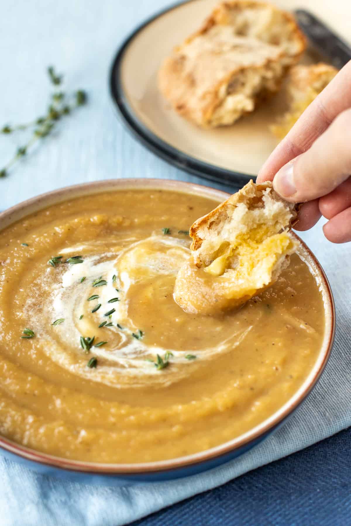 A hand dipping a piece of crusty bread and butter into a bowl of parsnip soup.