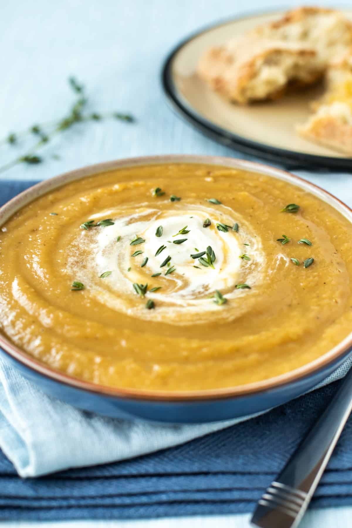 A bowl of roasted parsnip soup topped with a swirl of cream and fresh thyme leaves.