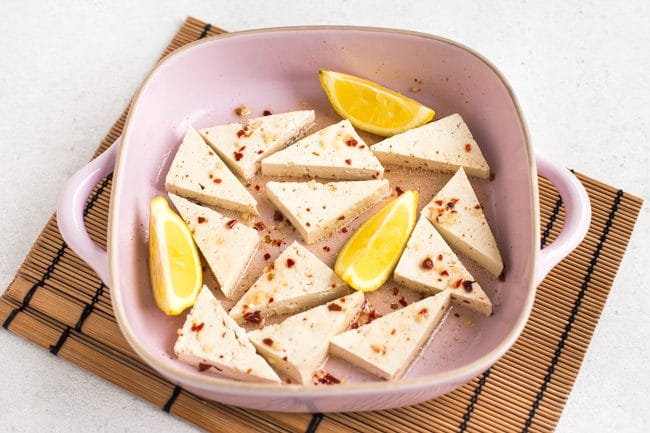 Tofu marinating in a dish with wedges of lemon
