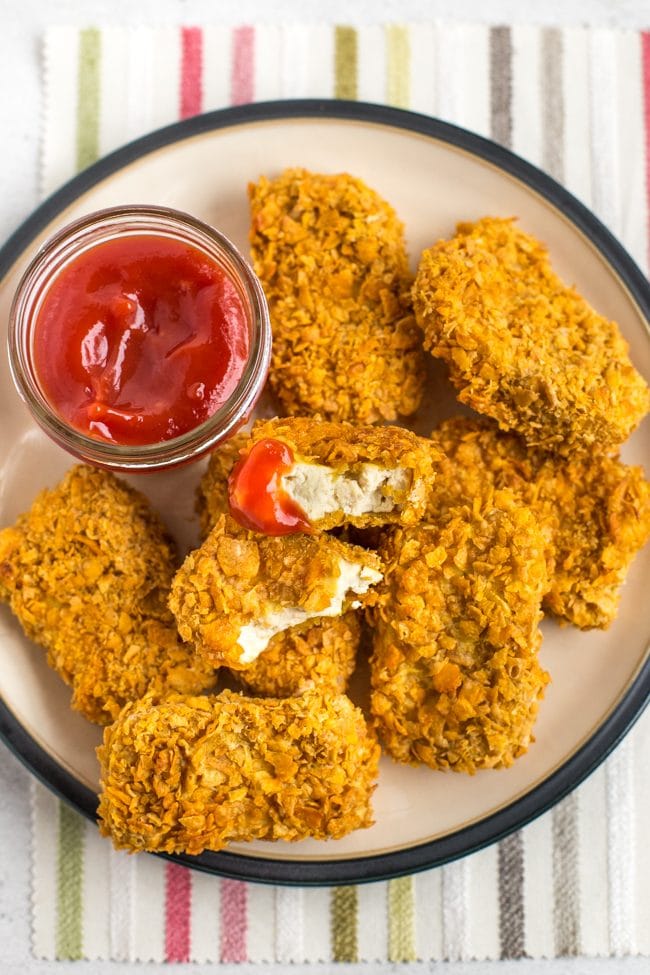 Portion of crispy baked tofu chicken nuggets on a plate with ketchup, with one broken in half