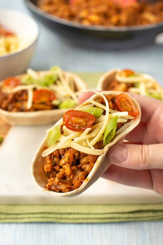 A hand holding up a lentil taco with toppings.