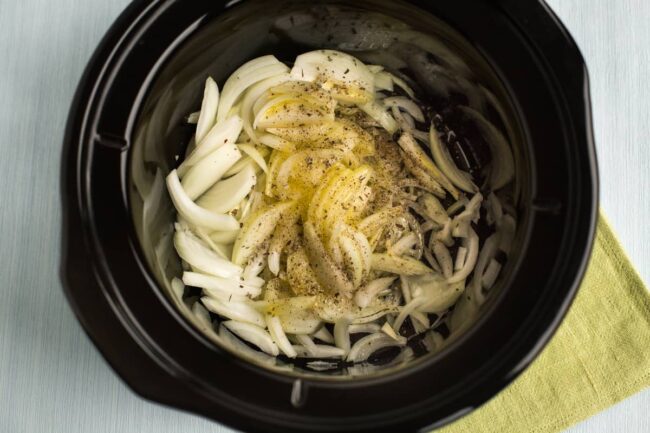 Sliced onions and dried sage in a slow cooker pot.