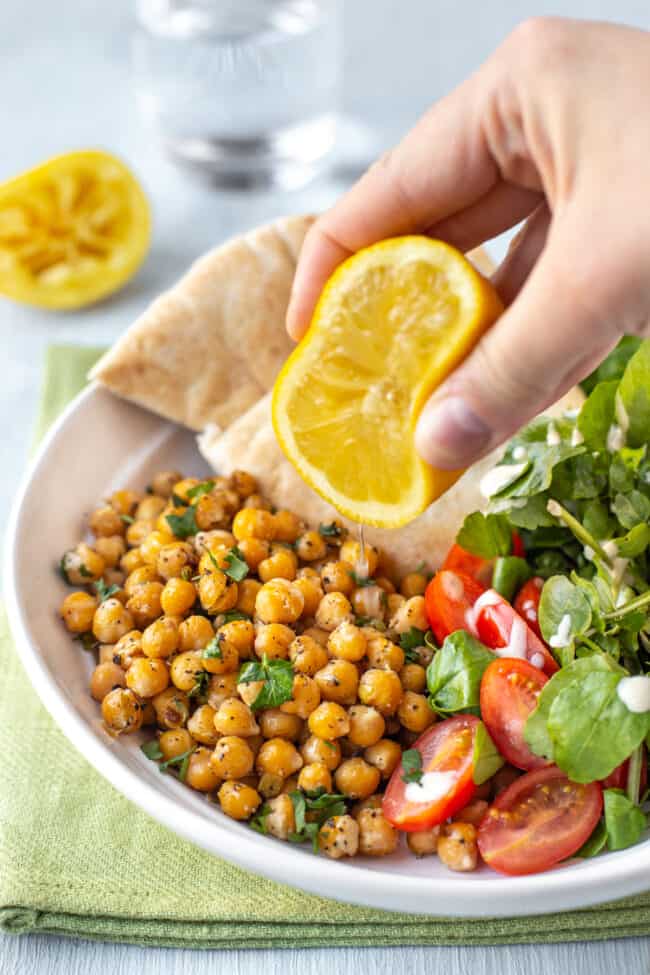 A hand squeezing fresh lemon juice onto some chickpeas and salad.