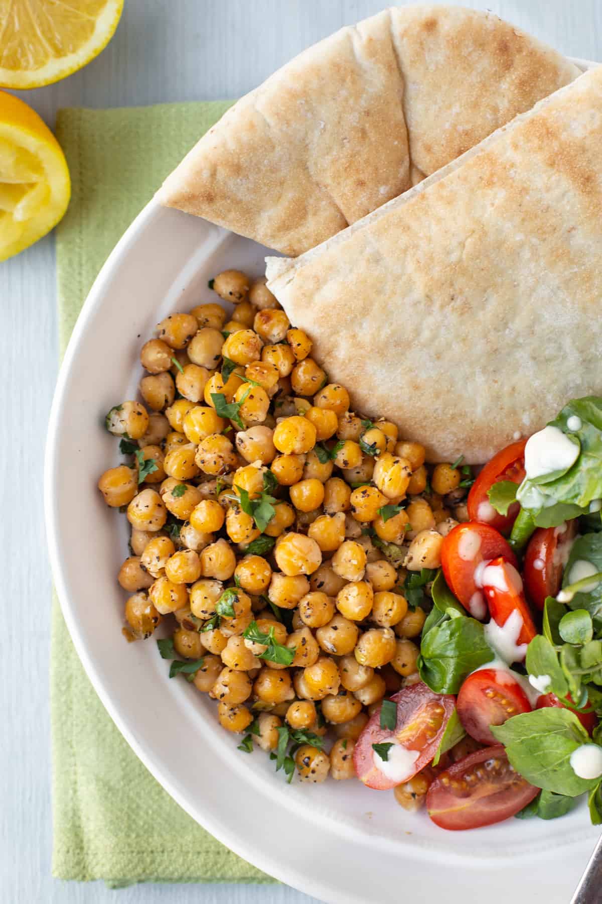 Lemon and black pepper chickpeas in a bowl with pitta bread, tomatoes and watercress.