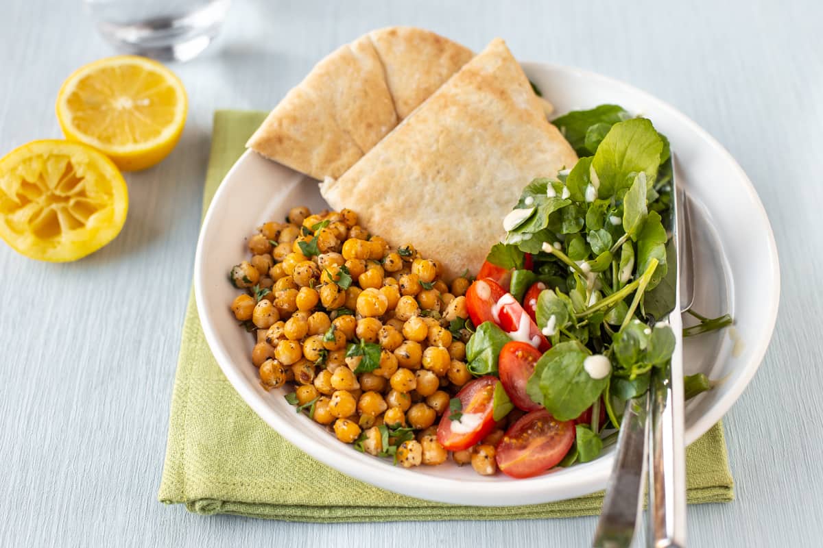 Lemon and black pepper chickpeas in a bowl with salad and pitta bread.
