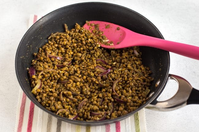 Brown lentils being cooked in a frying pan with red onion