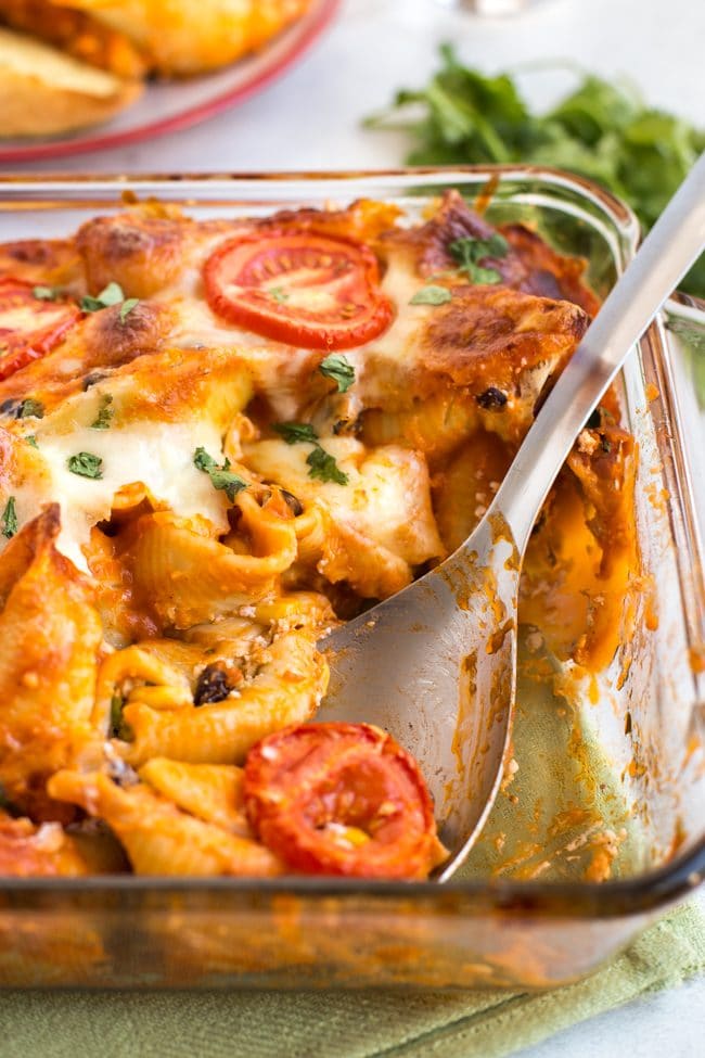 Cheesy enchilada stuffed pasta shells in a baking dish with a portion removed