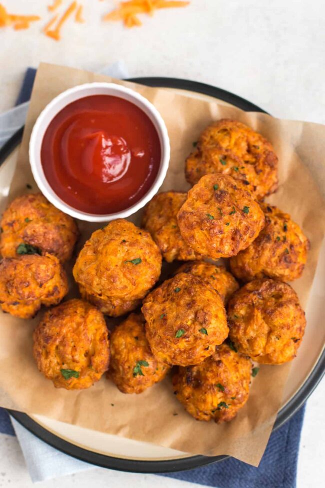 Pile of carrot and cheddar bites on a plate with a pot of ketchup.