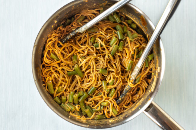 Peanut noodles in a pan with green beans.