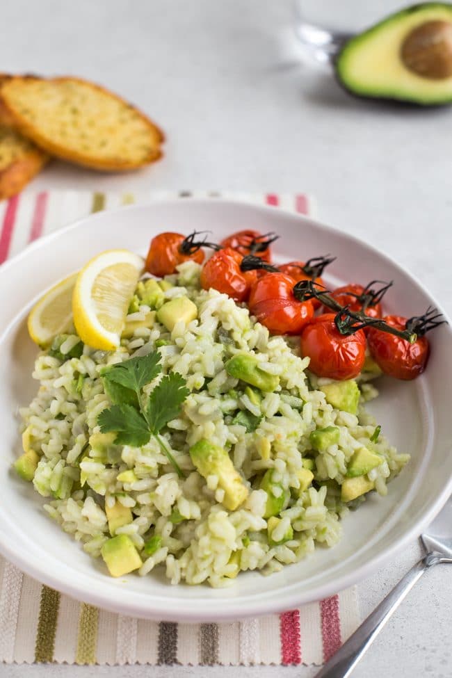 Portion of vegan avocado risotto in a bowl with lemon wedges and roasted tomatoes