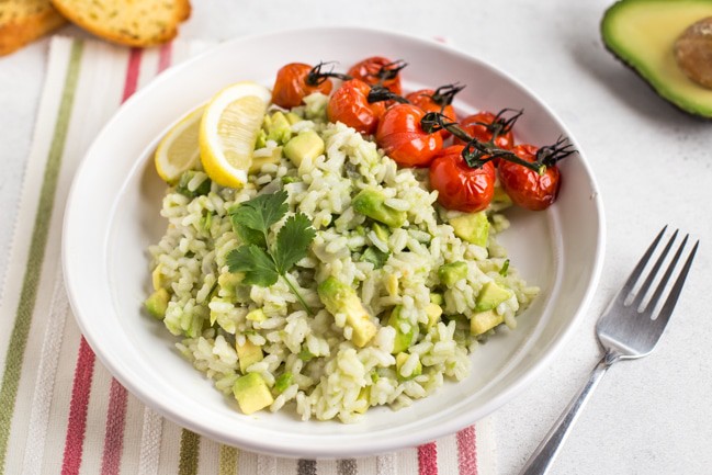 Portion of vegan avocado risotto in a bowl with lemon wedges and roasted tomatoes