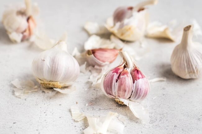 Several fresh heads of garlic with the papery skin partially removed to show the pink skin below.