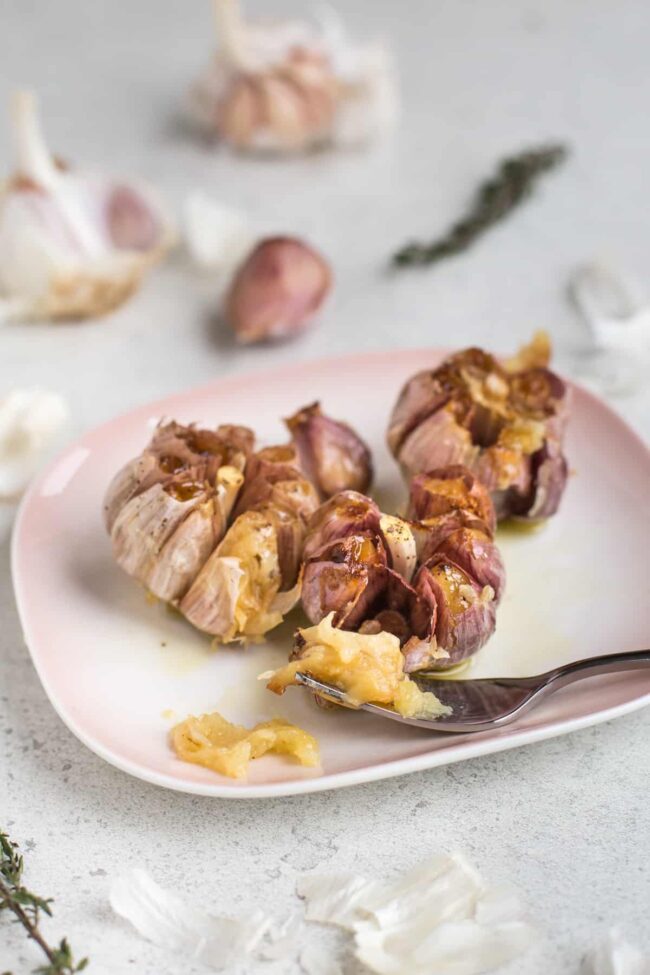 3 heads of roasted garlic on a pink plate with the garlic scooped out.