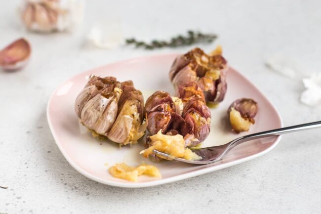 3 heads of roasted garlic on a pink plate.