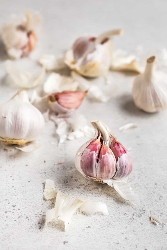Several heads of garlic with the papery skin partially removed to show the pink skin underneath.
