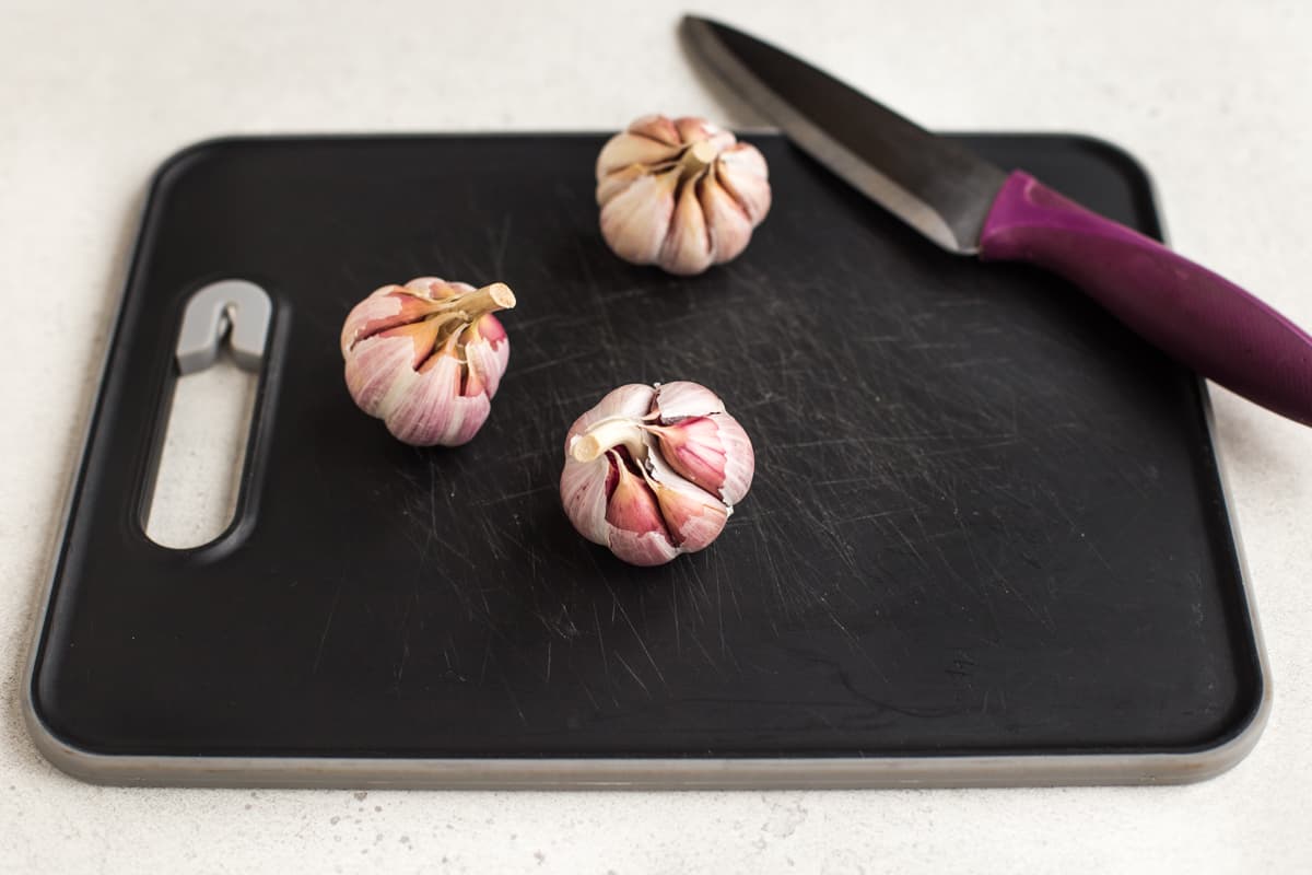 3 heads of garlic on a chopping board.
