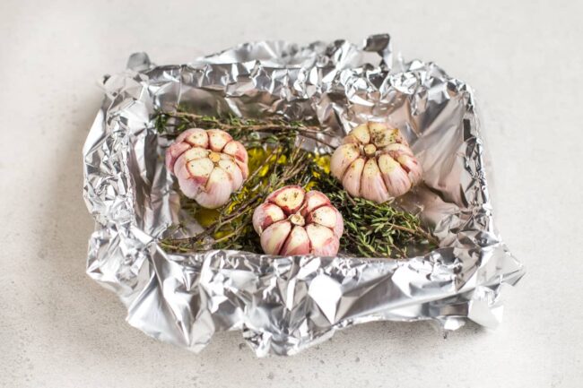 Garlic heads ready to roast in a foil lined dish with fresh thyme.