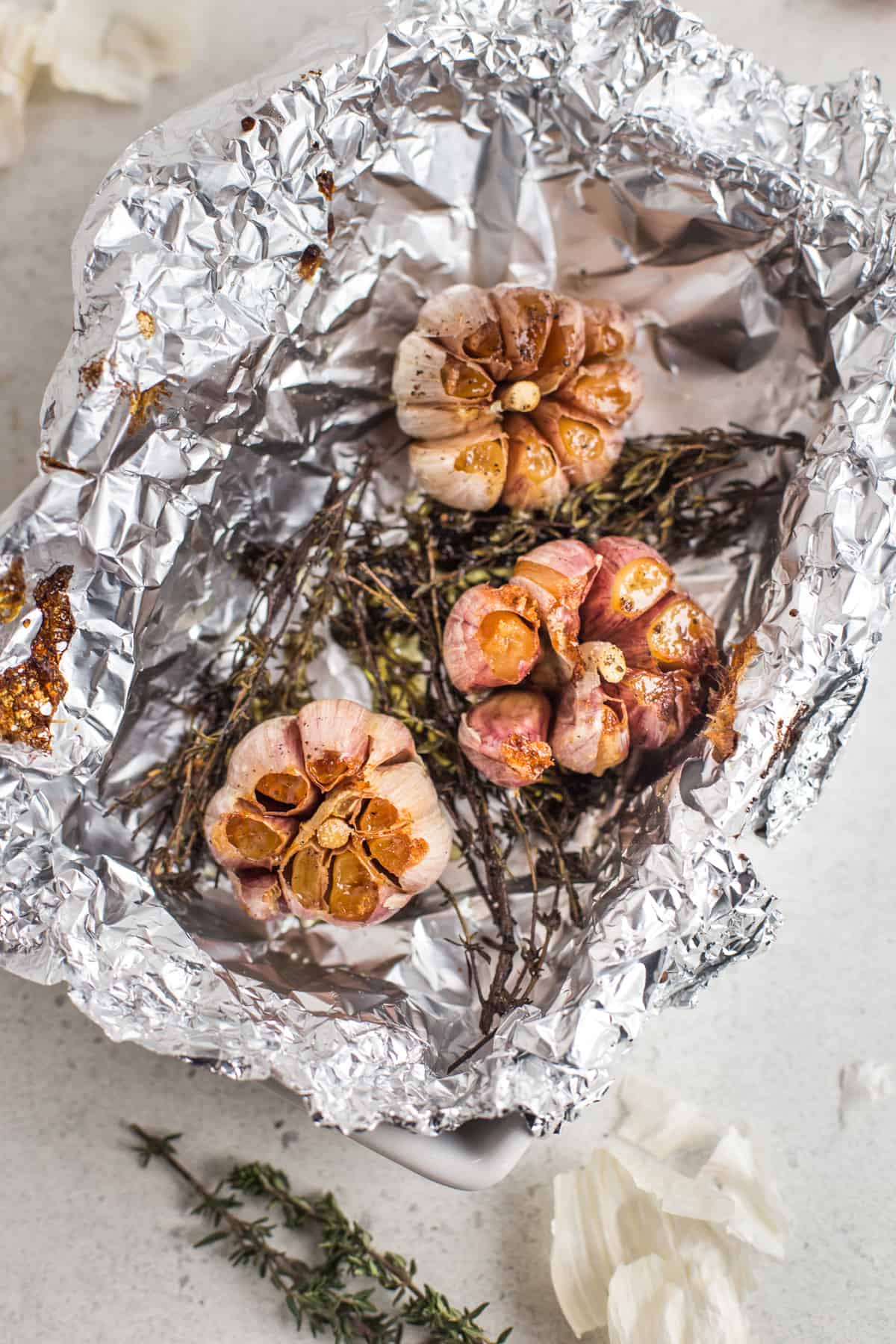 Roasted garlic on a bed of thyme in a foil lined dish.