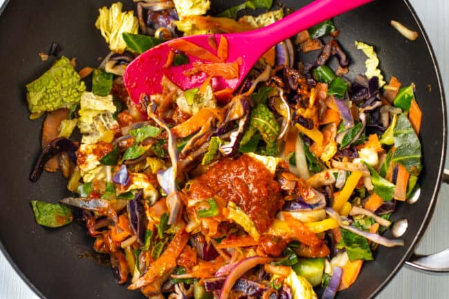 Stir fried vegetables in a wok with a dollop of red Thai curry paste.