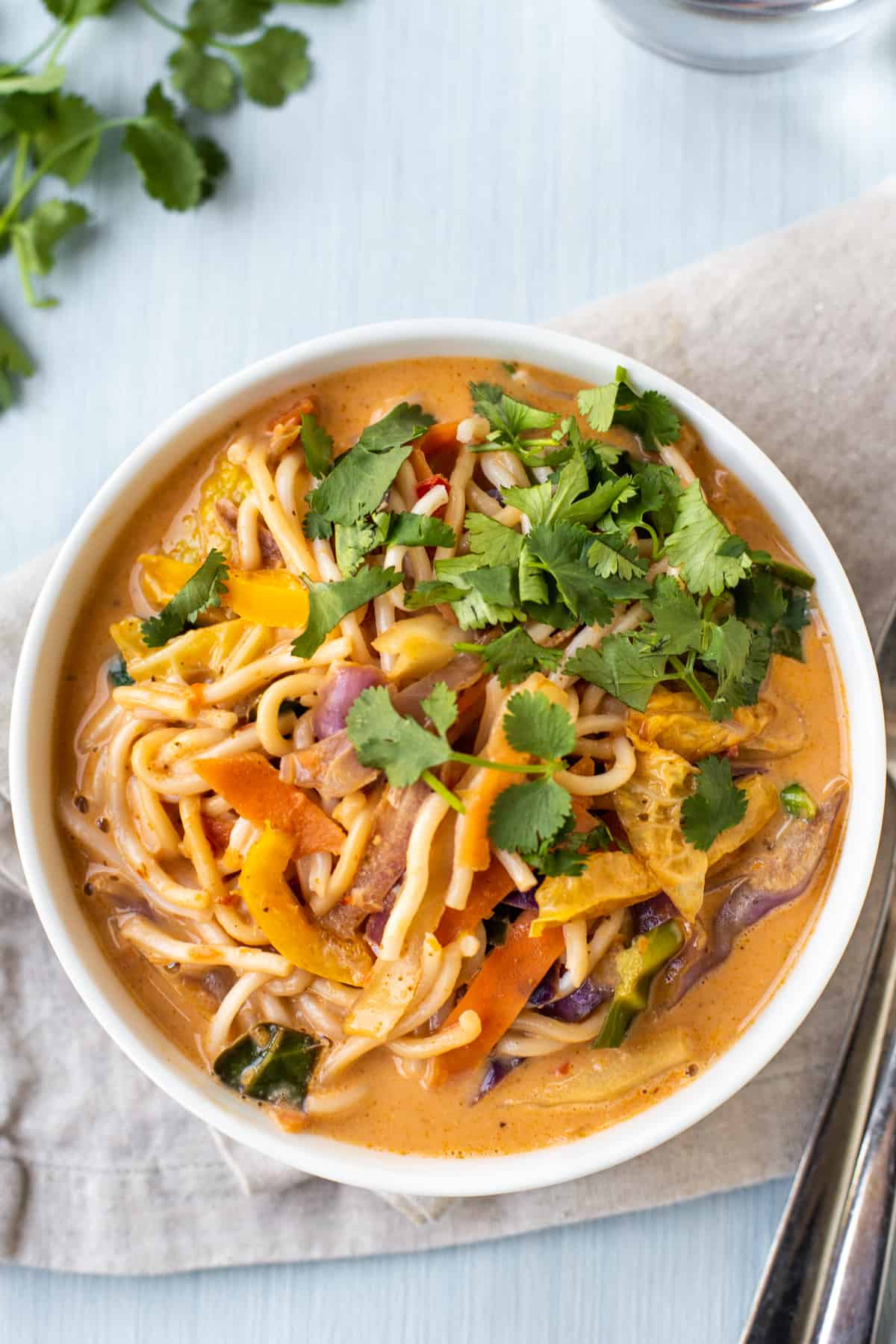 A bowl of red Thai curry noodle soup topped with fresh cilantro.