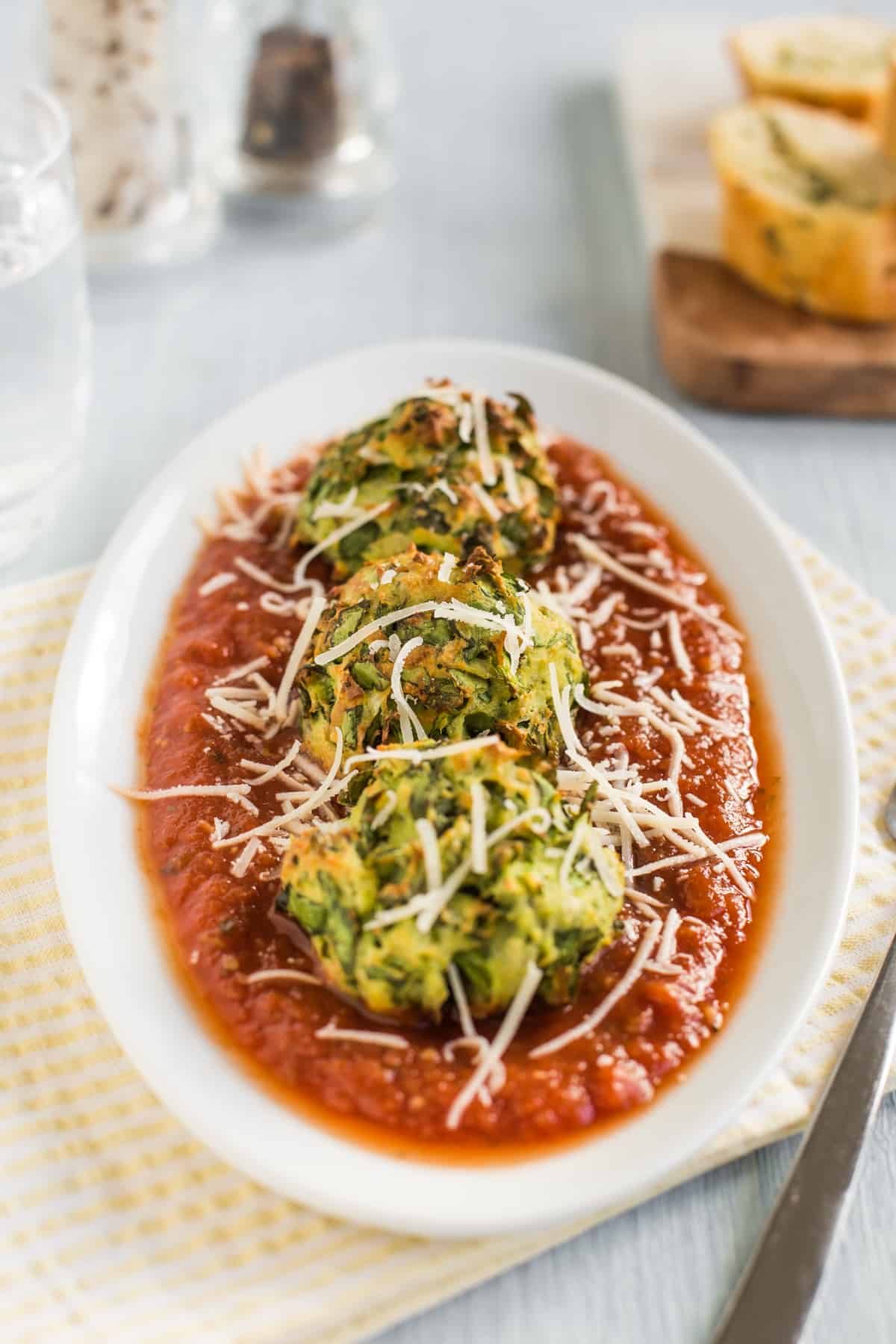 Portion of spinach and ricotta dumplings on a plate with tomato sauce and cheese