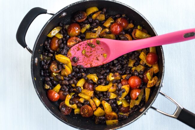 Veggies and black beans cooking in a frying pan.