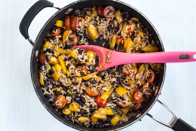 Veggie burrito bowl mixture in a frying pan, with rice, black beans, tomatoes and peppers.