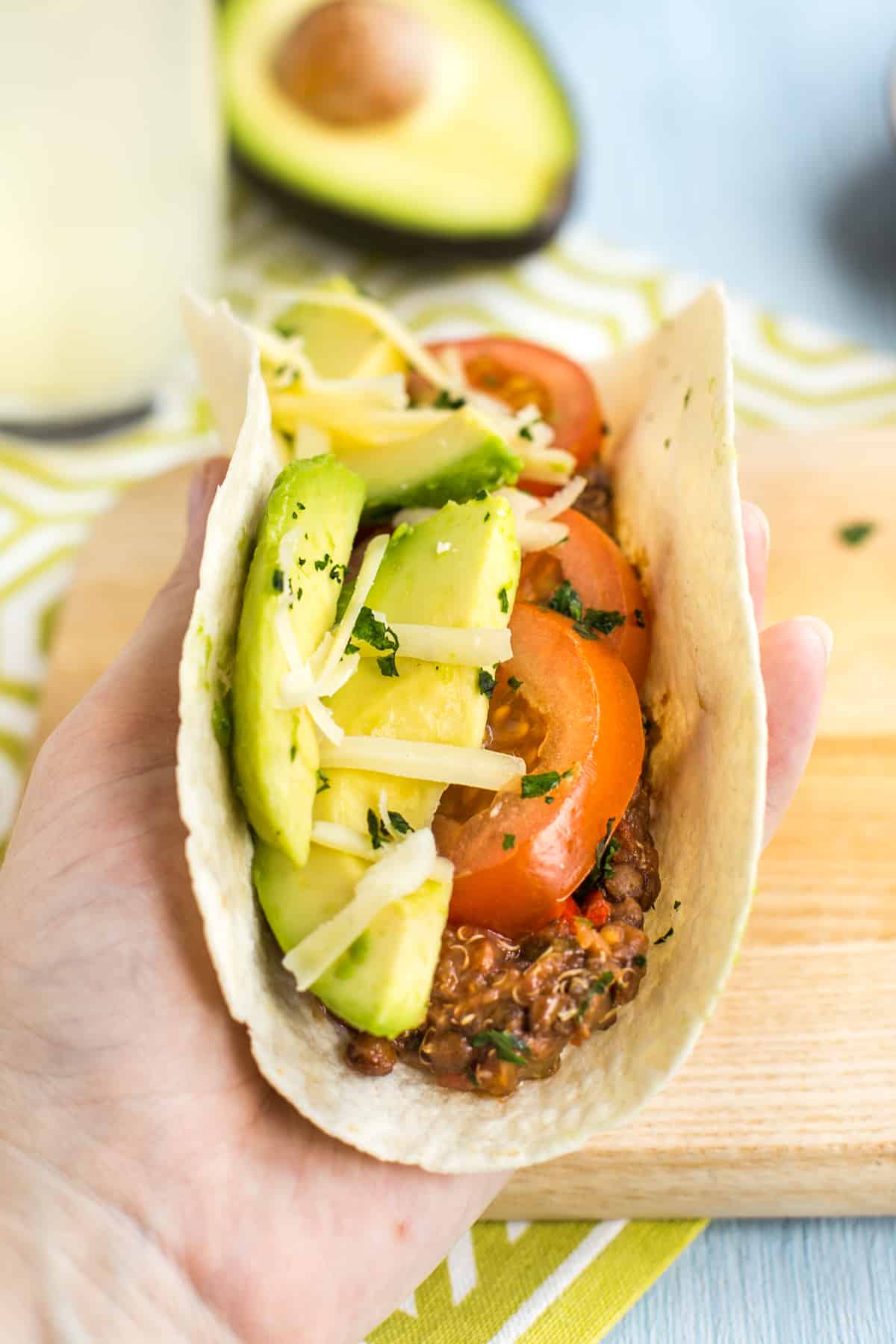 A lentil and quinoa taco topped with tomato and avocado, being held up in a hand.