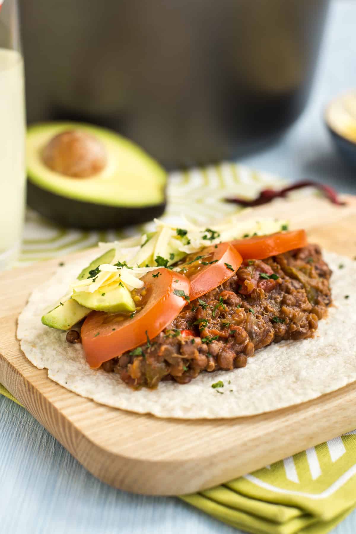 A lentil and quinoa taco topped with sliced tomatoes and avocado.
