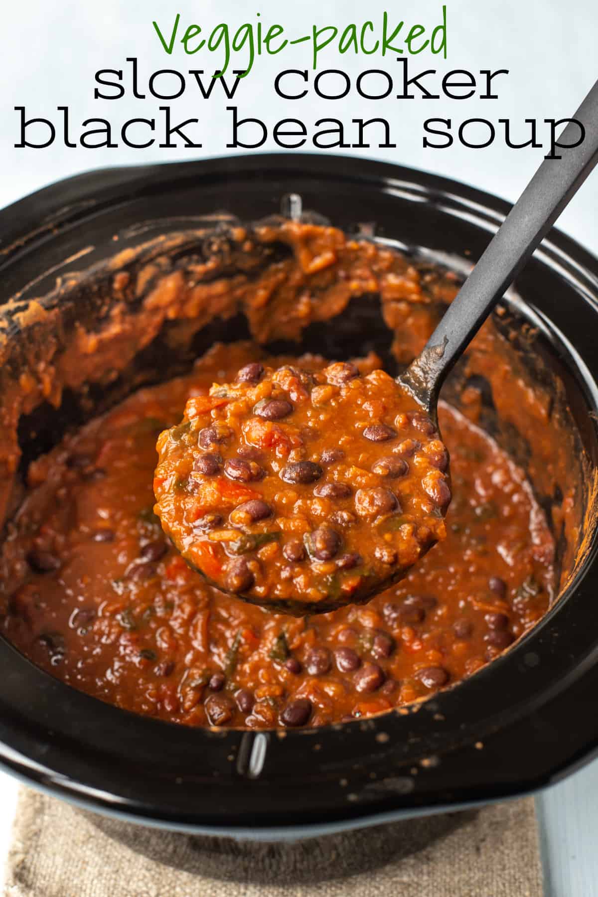 A ladle taking a scoop of black bean soup from a slow cooker.