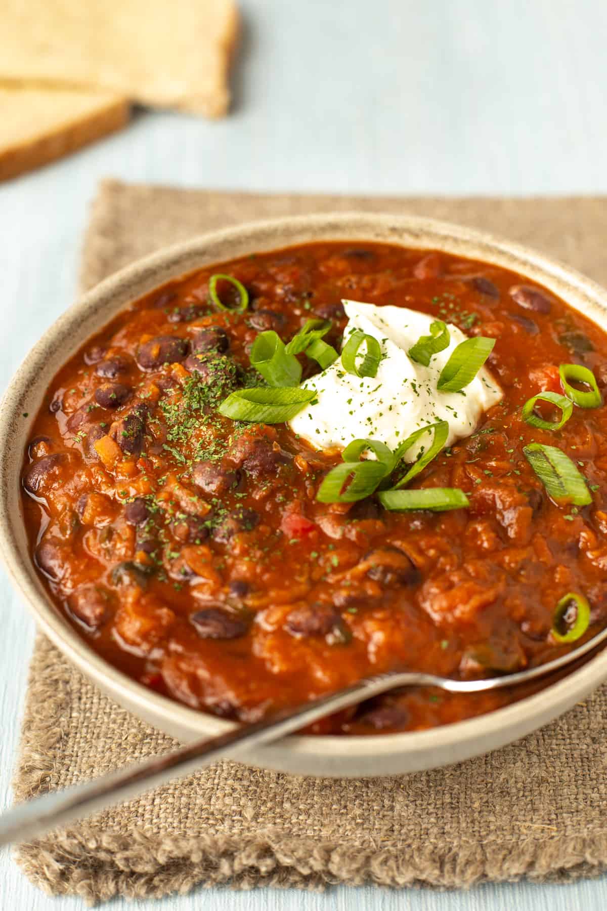 A bowlful of black bean soup topped with spring onions and sour cream.