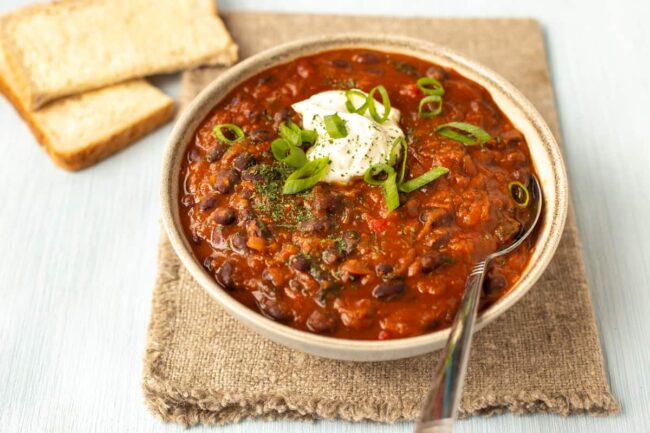 A bowl of black bean soup topped with spring onions and sour cream.