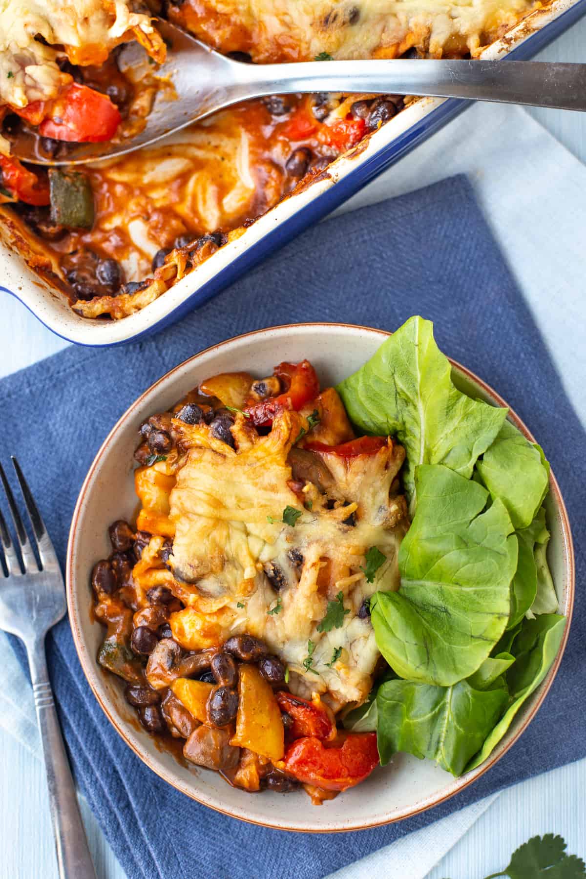 A portion of enchilada casserole with black beans, vegetables and a cheese topping.