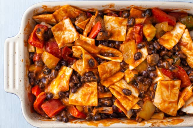 An uncooked enchilada casserole with pieces of tortilla and black beans in enchilada sauce.