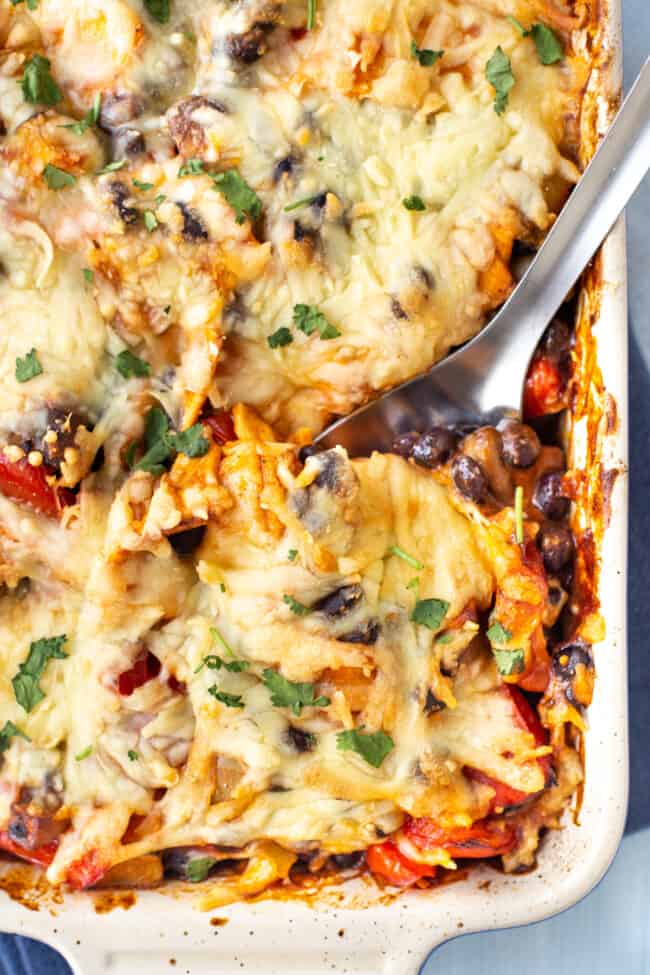 A large spoon digging into a baking dish of vegetarian enchilada casserole.