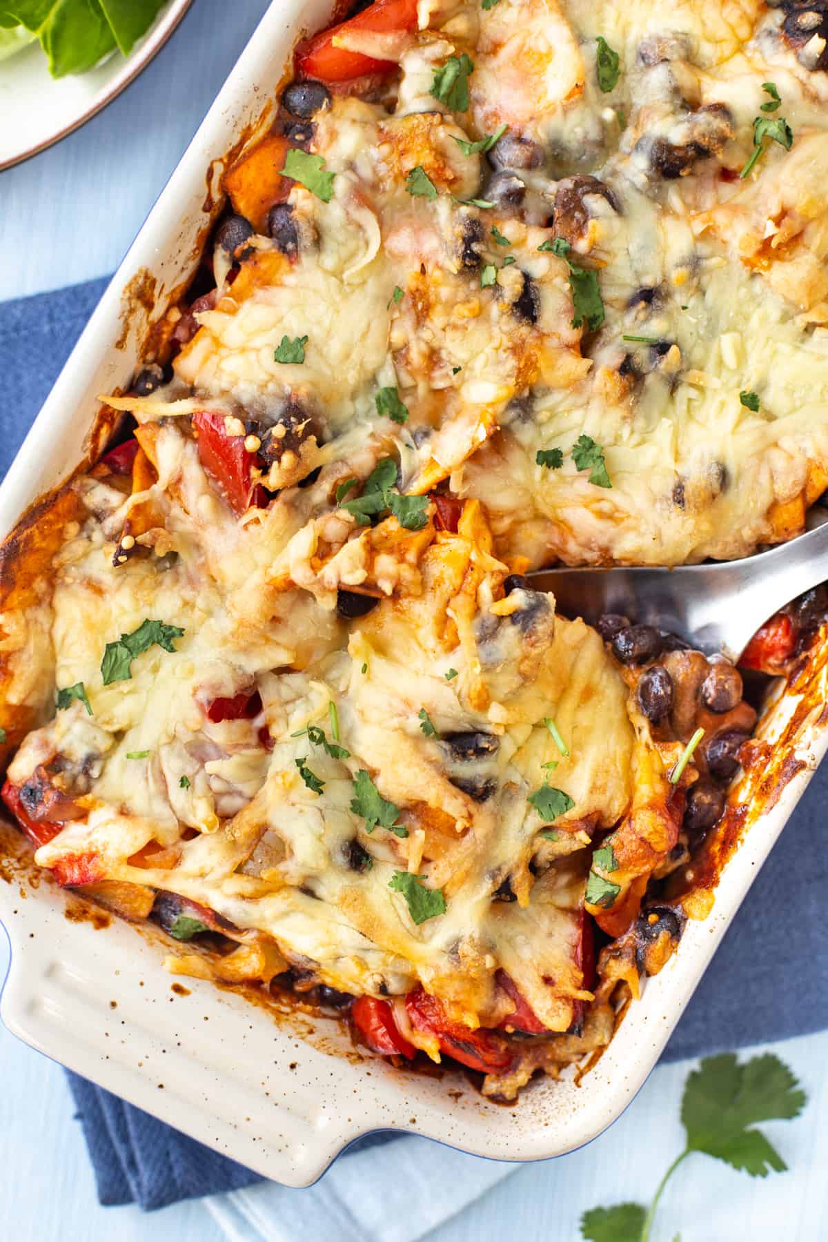 A cheesy enchilada casserole in a baking dish with a spoon.