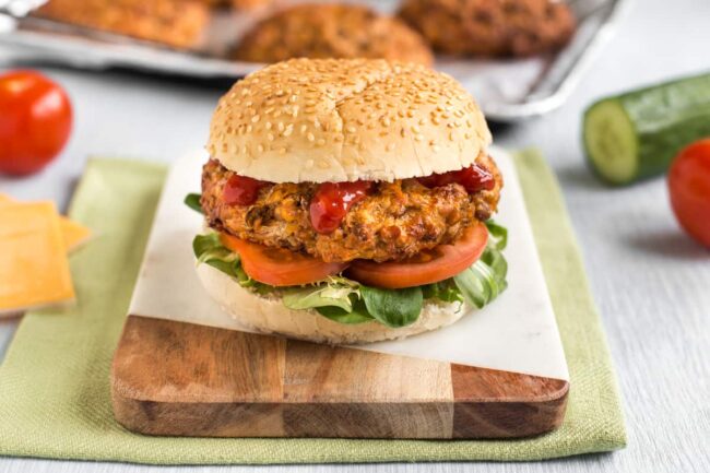 Cheesy lentil burgers in a bun with lettuce and tomato.